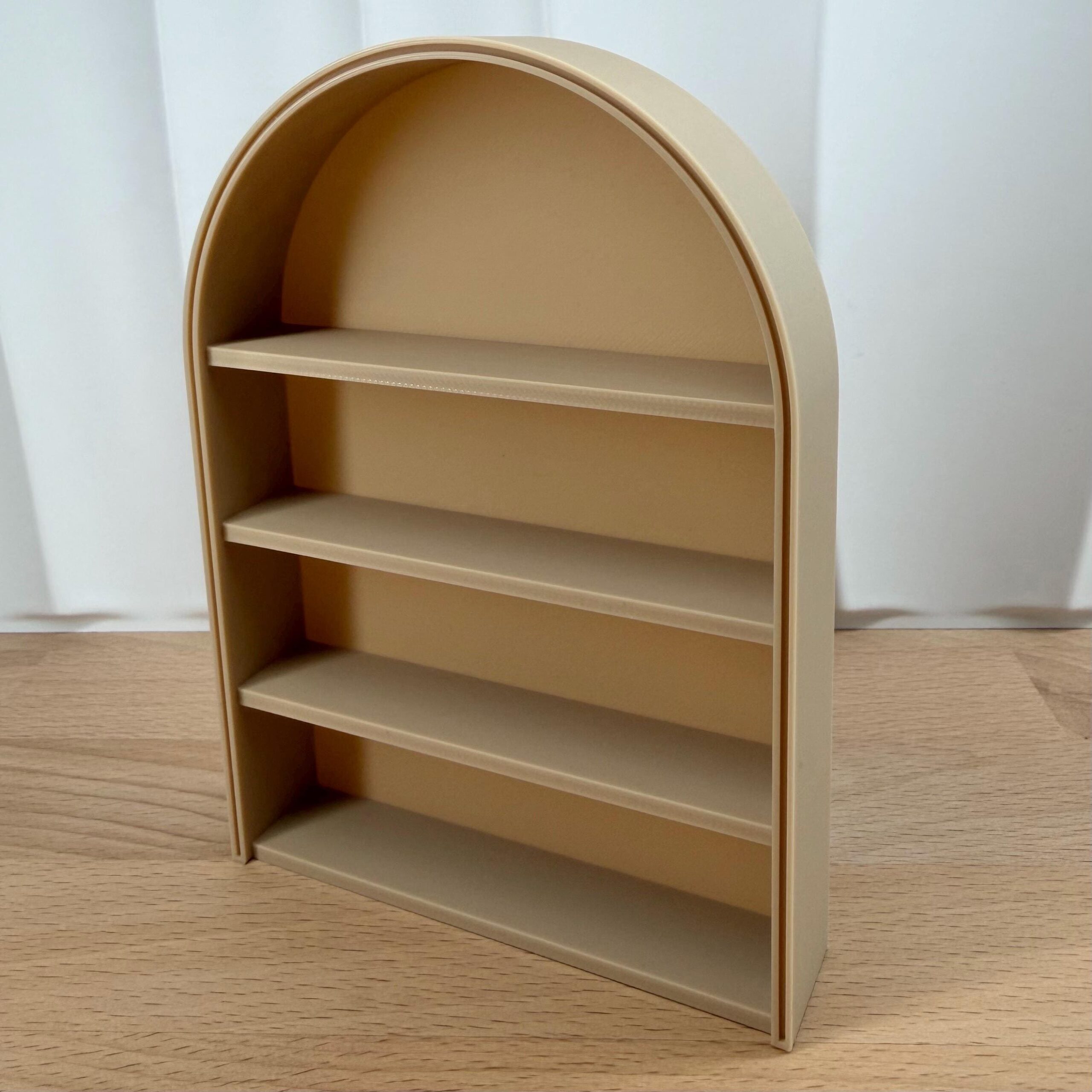 Empty 3D print 1:12 scale arched anxiety bookshelf in beige on a wooden table. Support-free STL file model for miniature dollhouse furniture.